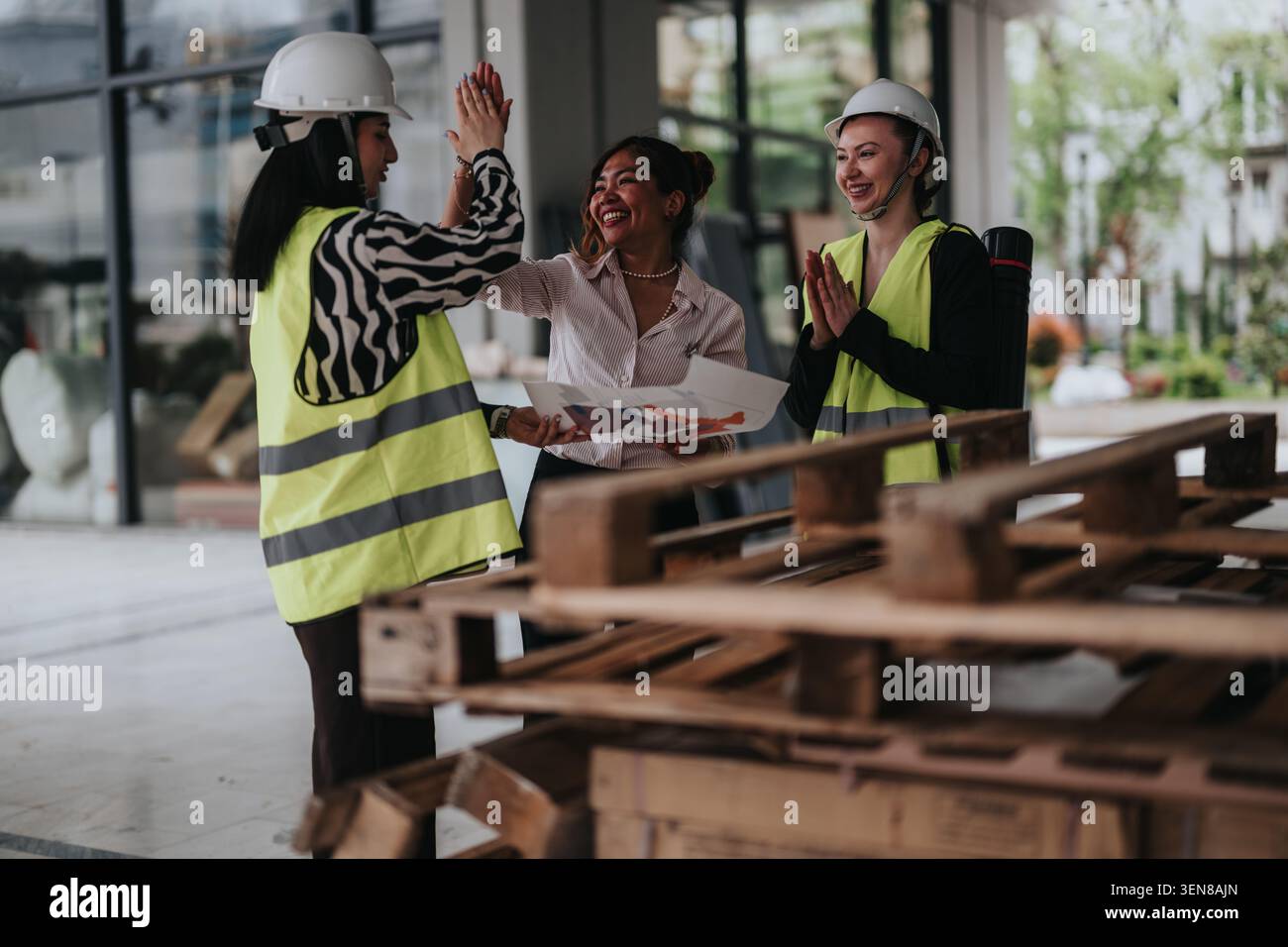 Three female construction workers in hard hats and safety vests celebrating while reviewing building plans Stock Photo