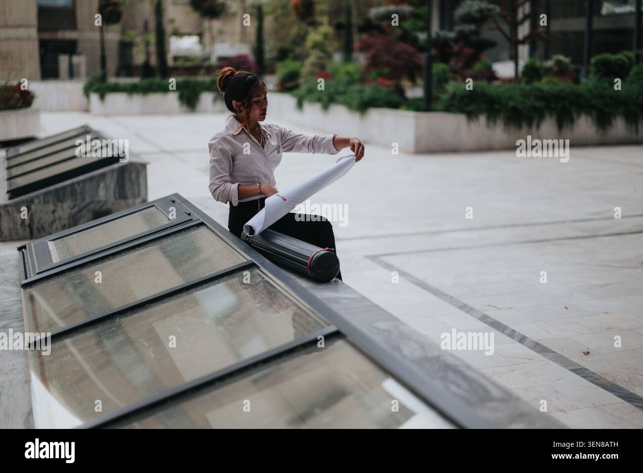 Young architect reviewing blueprints outdoors on a modern office plaza during a work break Stock Photo