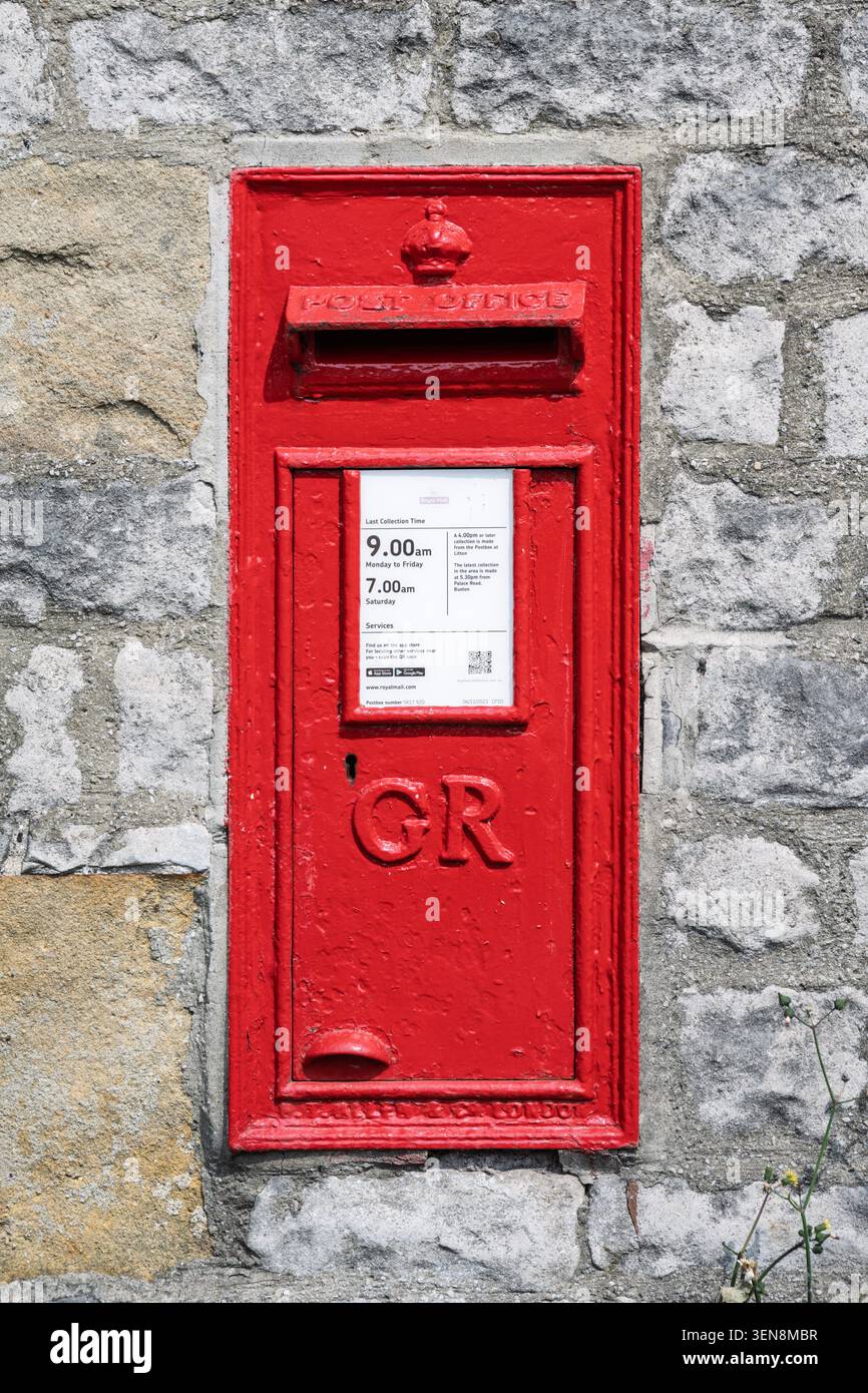 Close-up vertical detail of a historic red George V post box set into a traditional limestone wall in Tideswell village Stock Photo