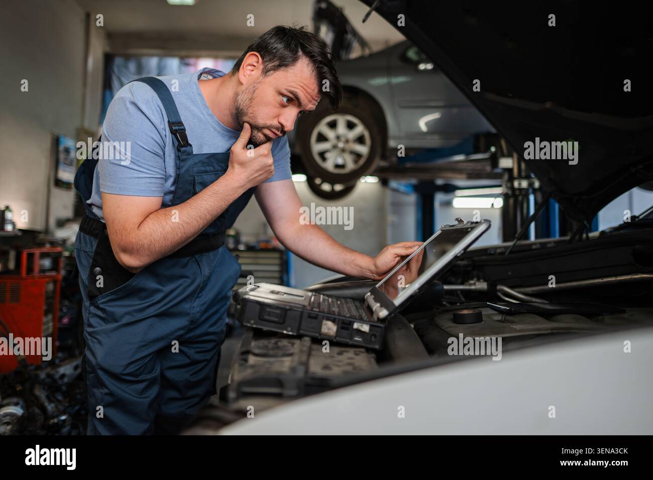 Auto mechanic using a computer to diagnose a car engine problem in a repair shop Stock Photo