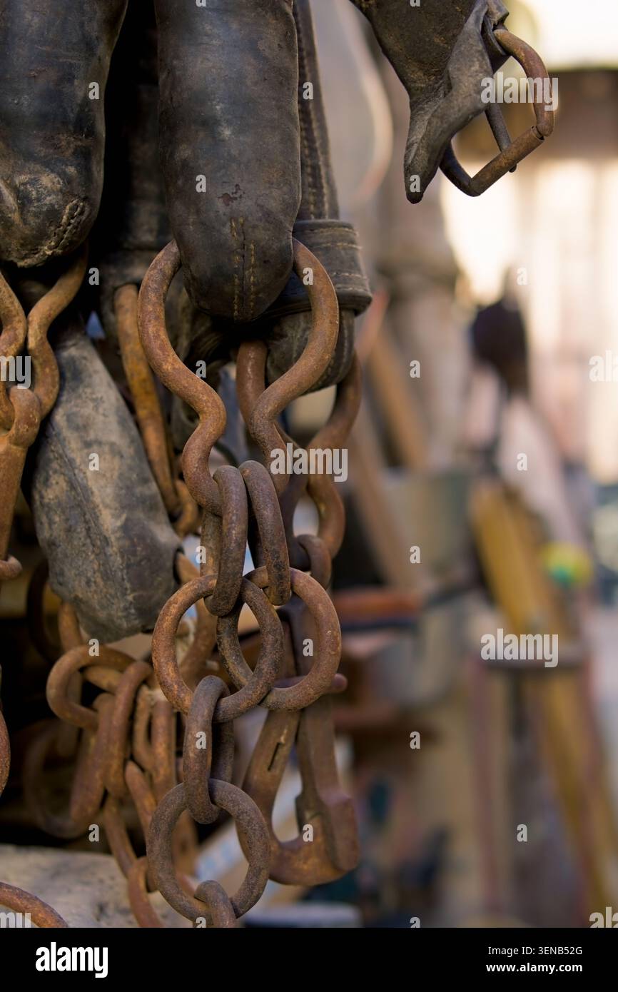 Rusty chains hang heavy from worn leather boots. Worn leather straps suggest rugged use. Background blur hints at outdoor workshop setting. Texture de Stock Photo