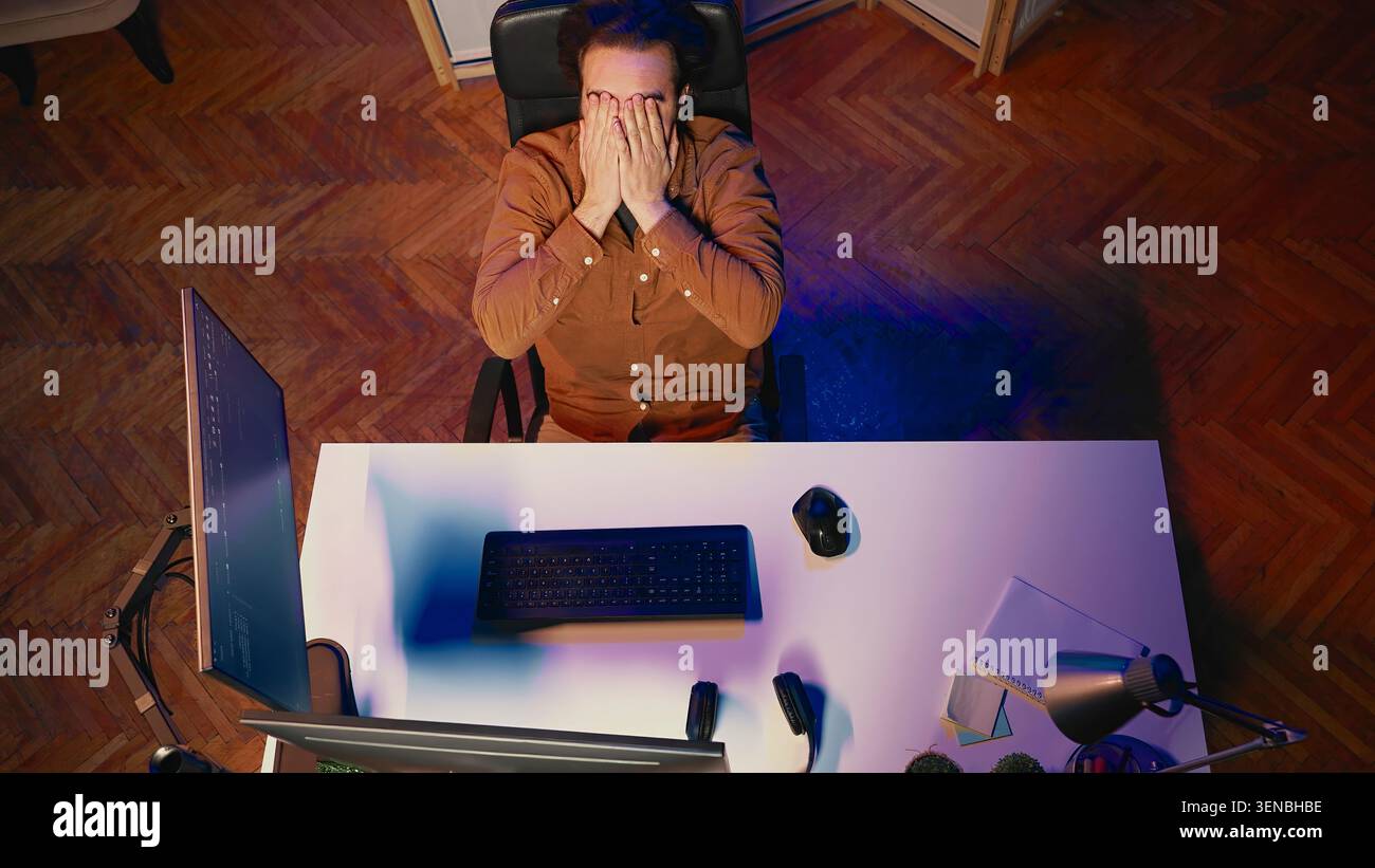 Top-down view of software engineer putting face in hands in frustration while updating binary code script on computer, receiving errors. IT worker exasperated by annoying bugs while programming. Stock Photo