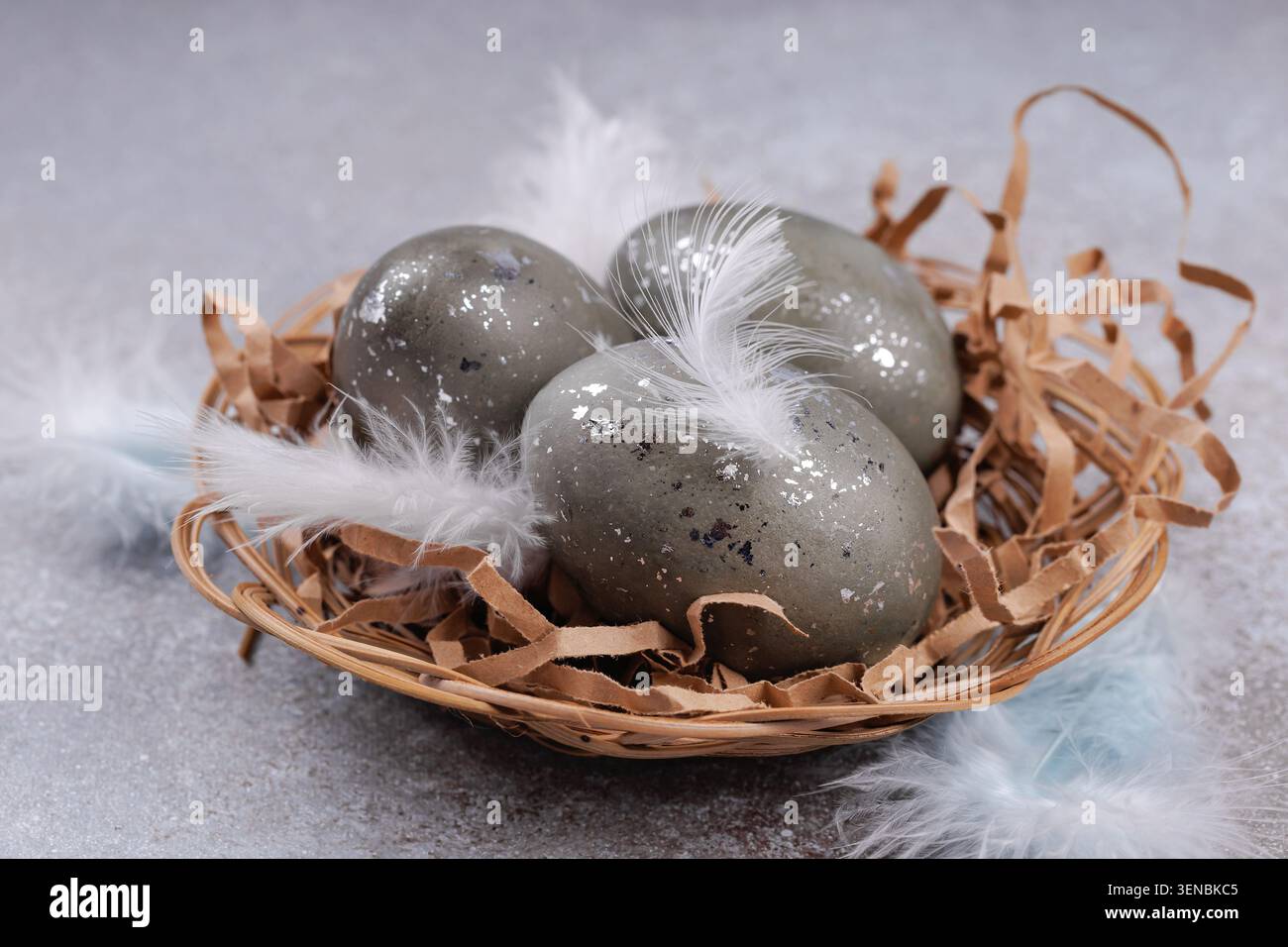 Easter eggs in wicker nest with feathers rustic background Stock Photo