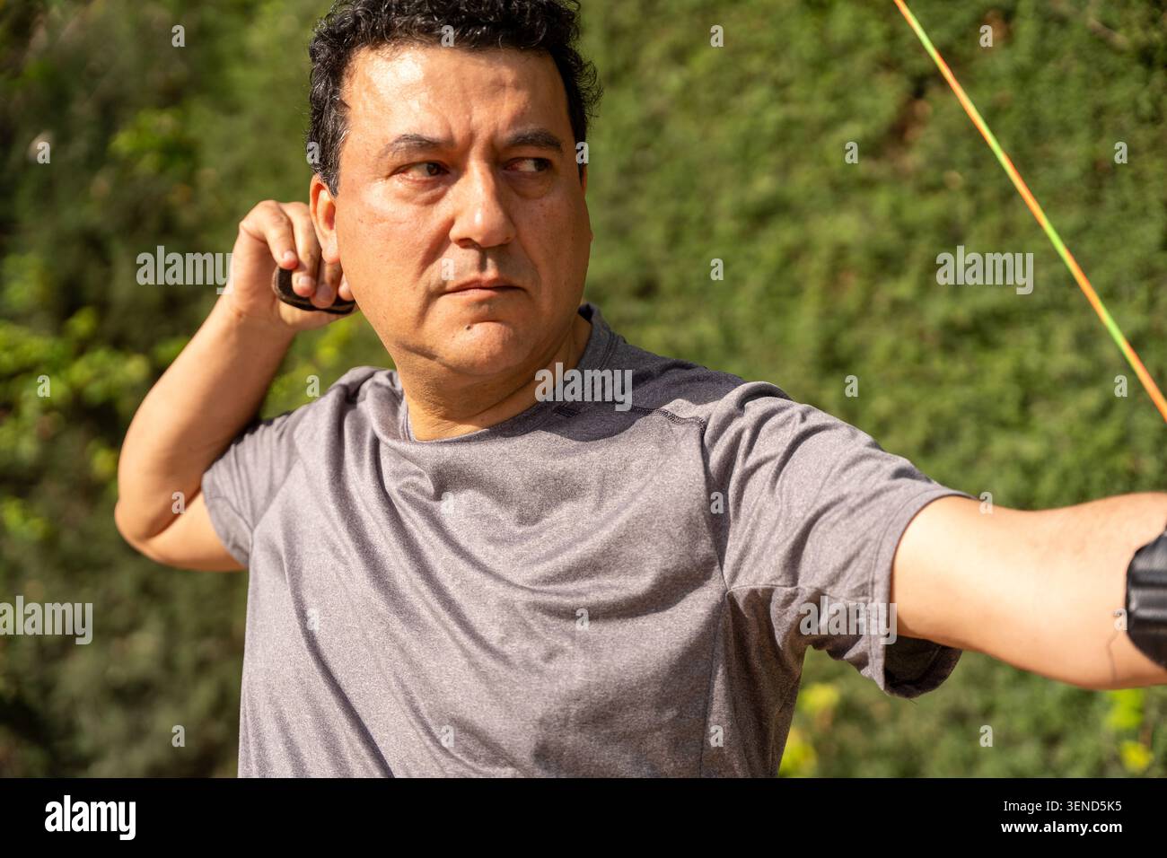 Man focusing and concentrating while shooting a bow and arrow during outdoor training Stock Photo