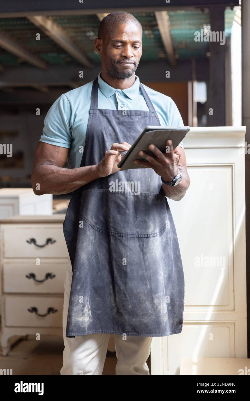 African American man using digital tablet and inspecting wooden cabinets in workshop Stock Photo
