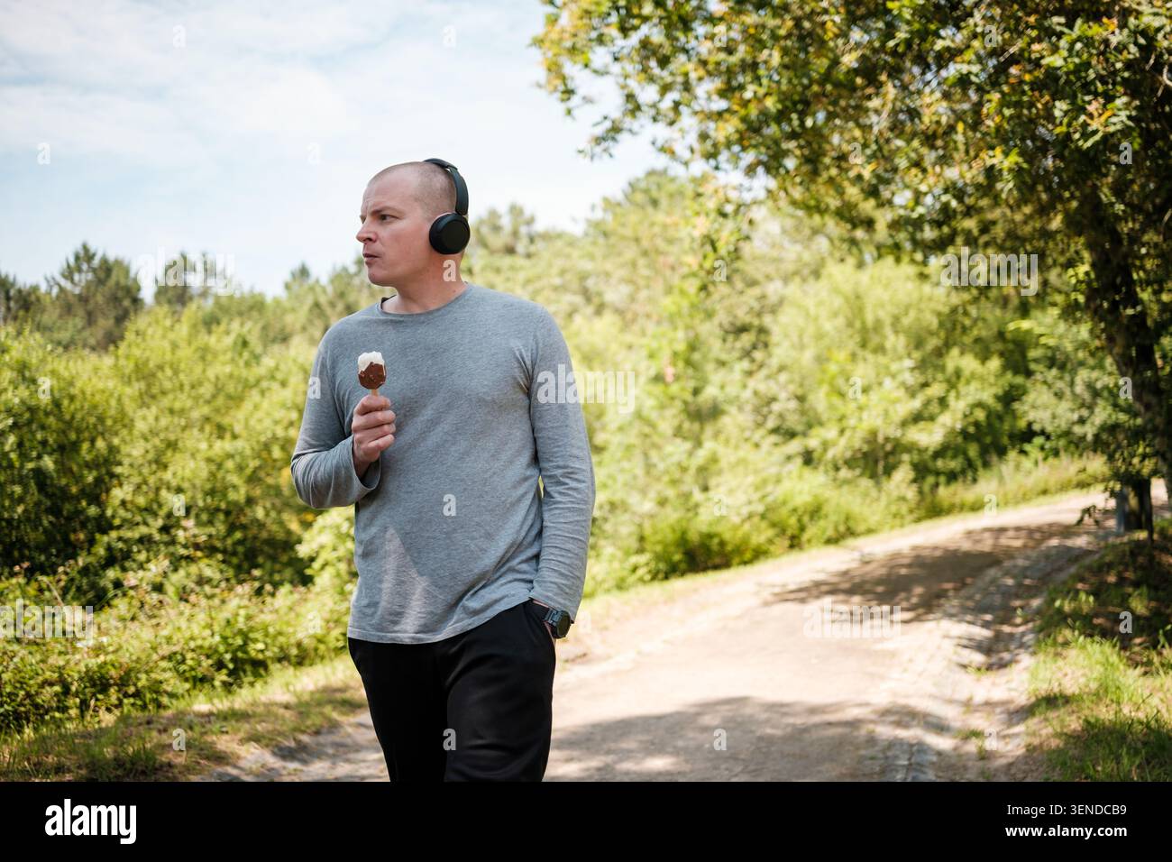 Man enjoying a summer walk in the park while eating ice cream on a stick and listening to music Stock Photo