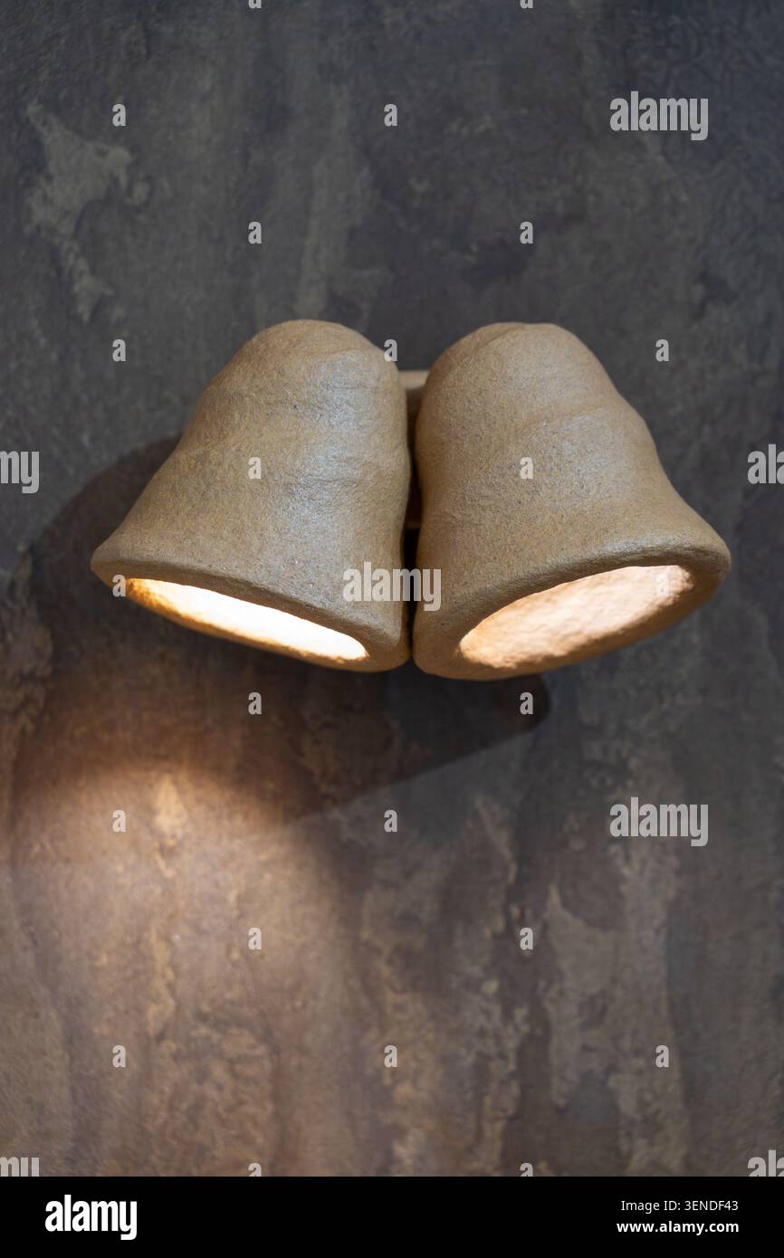 Handcrafted dual ceramic wall sconce with warm LED illumination mounted on textured dark plaster wall in modern minimalist interior Stock Photo