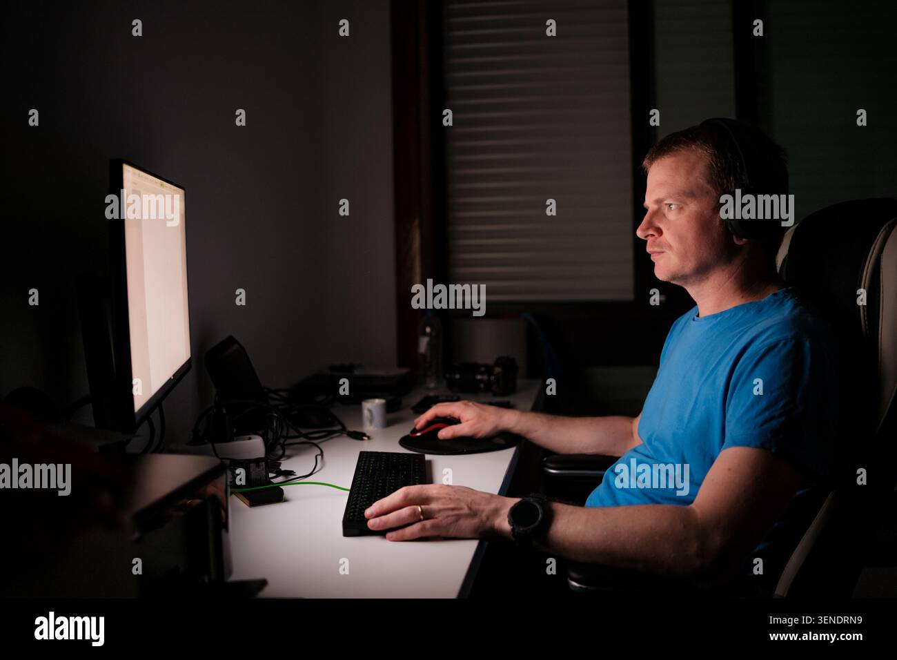 Man wearing headphones working on computer, typing on keyboard and using mouse Stock Photo