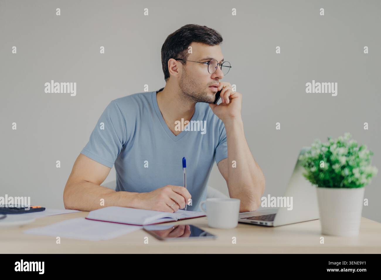 Young man writes notes beside laptop while working at home desk Stock Photo