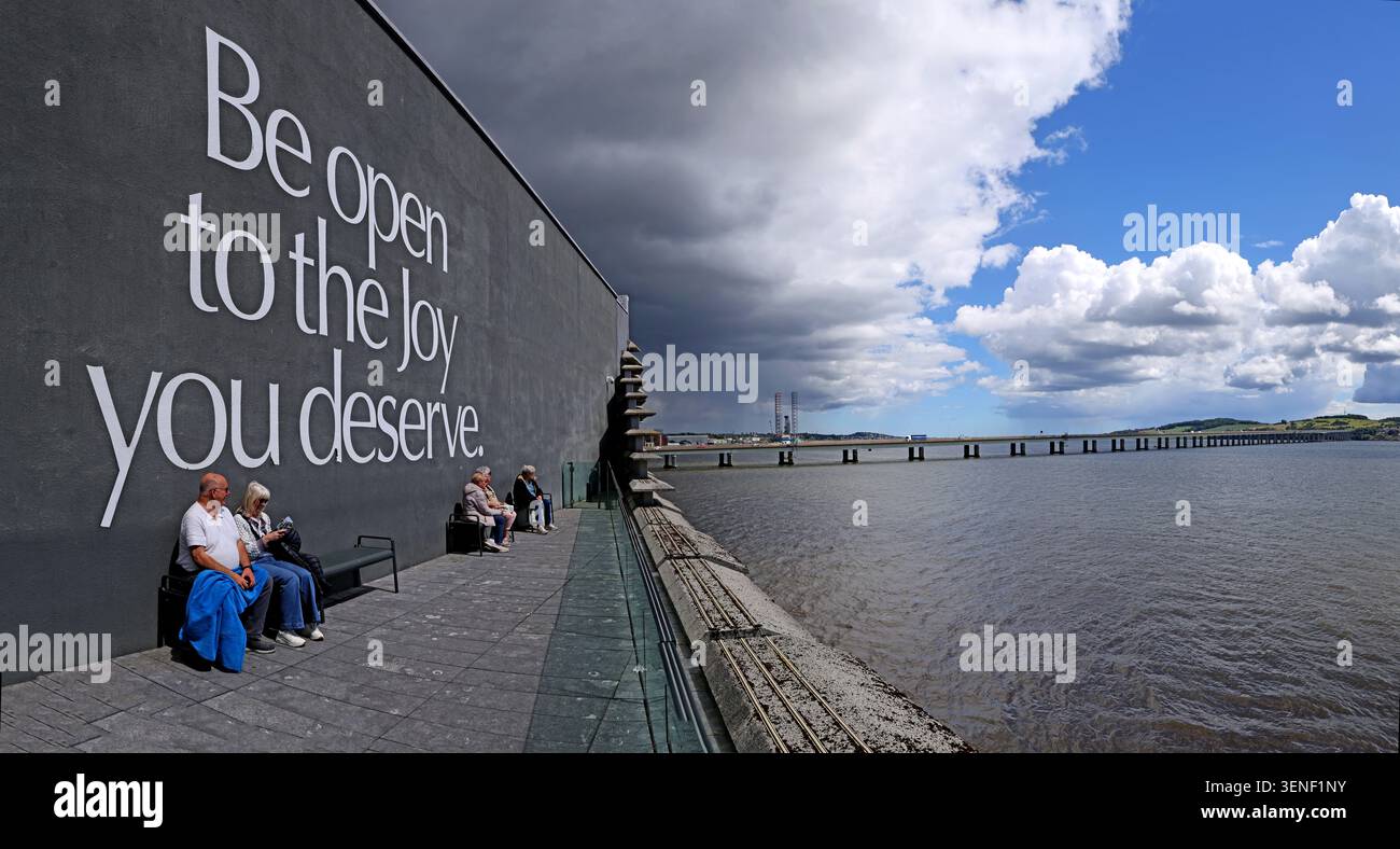 Visitors relaxing outside V&A Dundee beside the Be open to the joy wall, overlooking the River Tay in Scotland Stock Photo