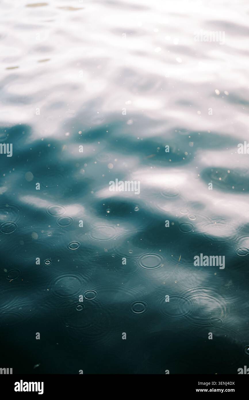 Raindrops Creating Ripples on Calm Water Surface Stock Photo