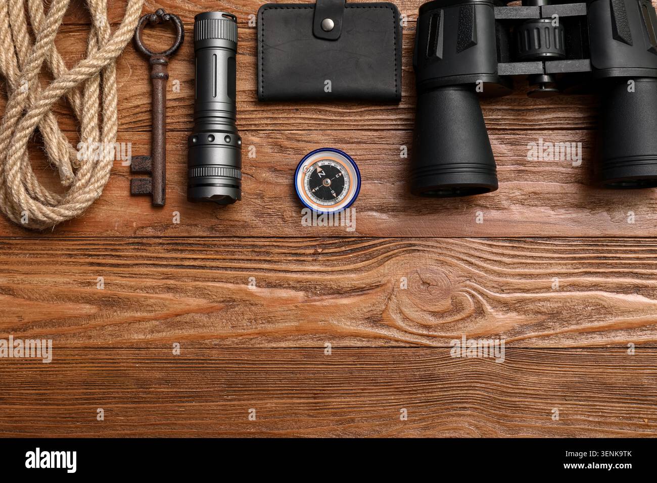 Adventure exploration gear flat lay with binoculars, compass, flashlight, rope, and old key on rustic wooden background Stock Photo