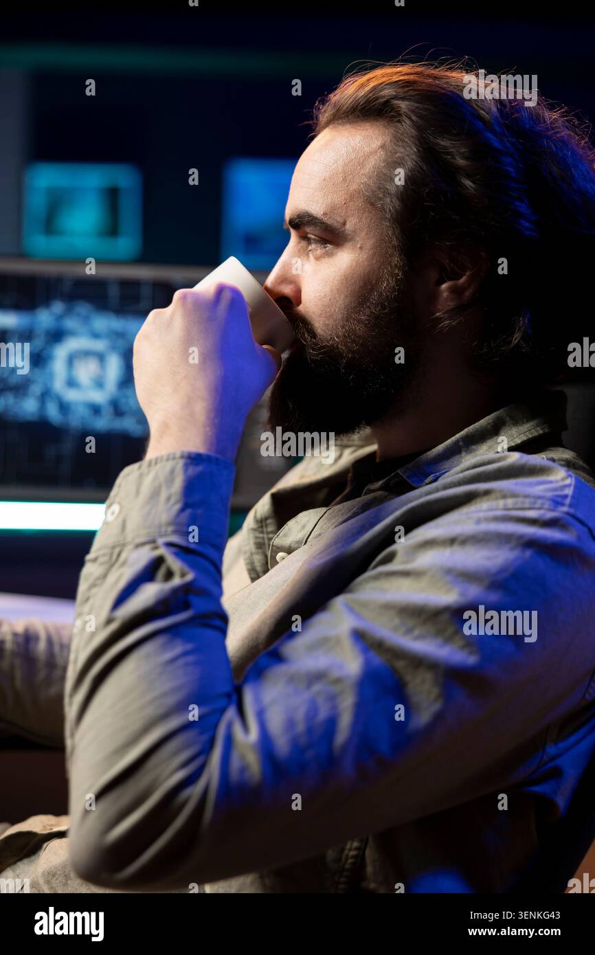 Developer drinking coffee updating artificial intelligence machine learning algorithm on PC desktop at home, IT specialist in apartment office enjoying hot beverage while upgrading AI. Stock Photo