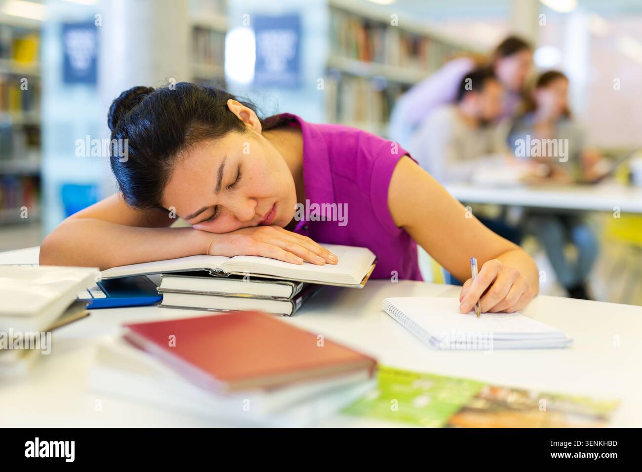 Tired woman lying on books at library Stock Photo