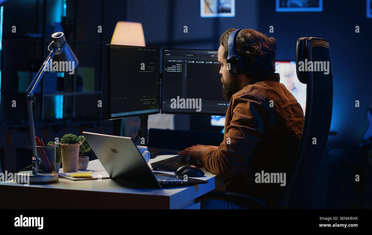 Engineer typing code in apartment office, using javascript programming language to develop software application. IT admin using multimonitor desktop setup and notebook to finish tasks, camera A. Stock Photo