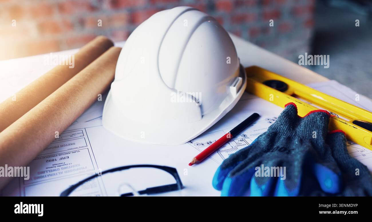 Helmet, architecture and tools in empty office with engineering gloves, blueprint or design. Construction, equipment and safety ppe at building site Stock Photo