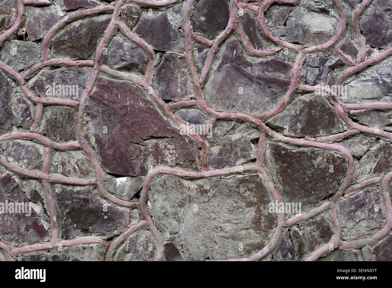 Dark stone wall texture with decorative pink mortar joints. Stock Photo