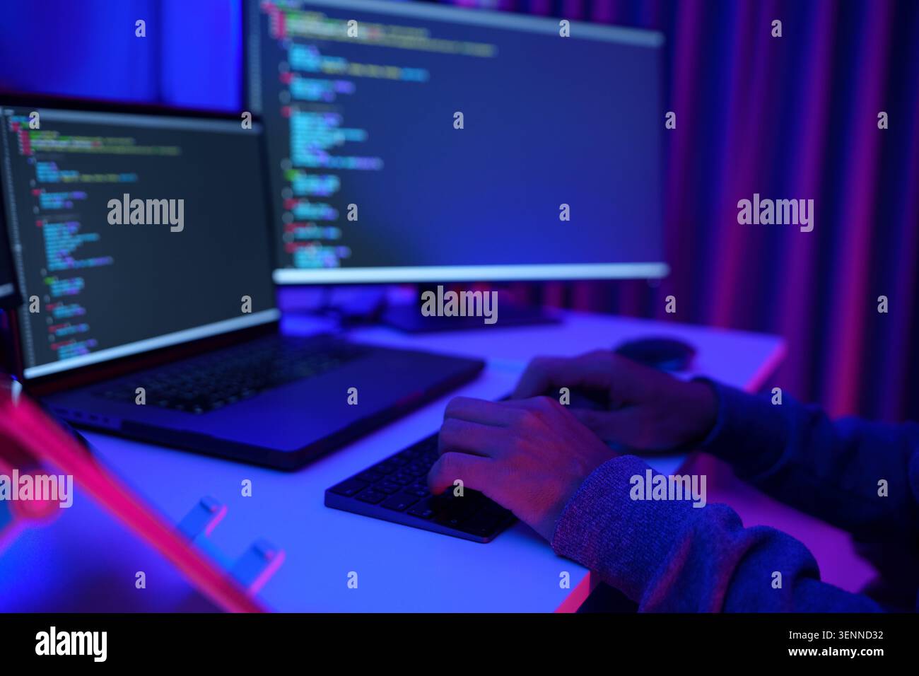 Programmer Working at Dual Monitors in Neon Lit Office Stock Photo