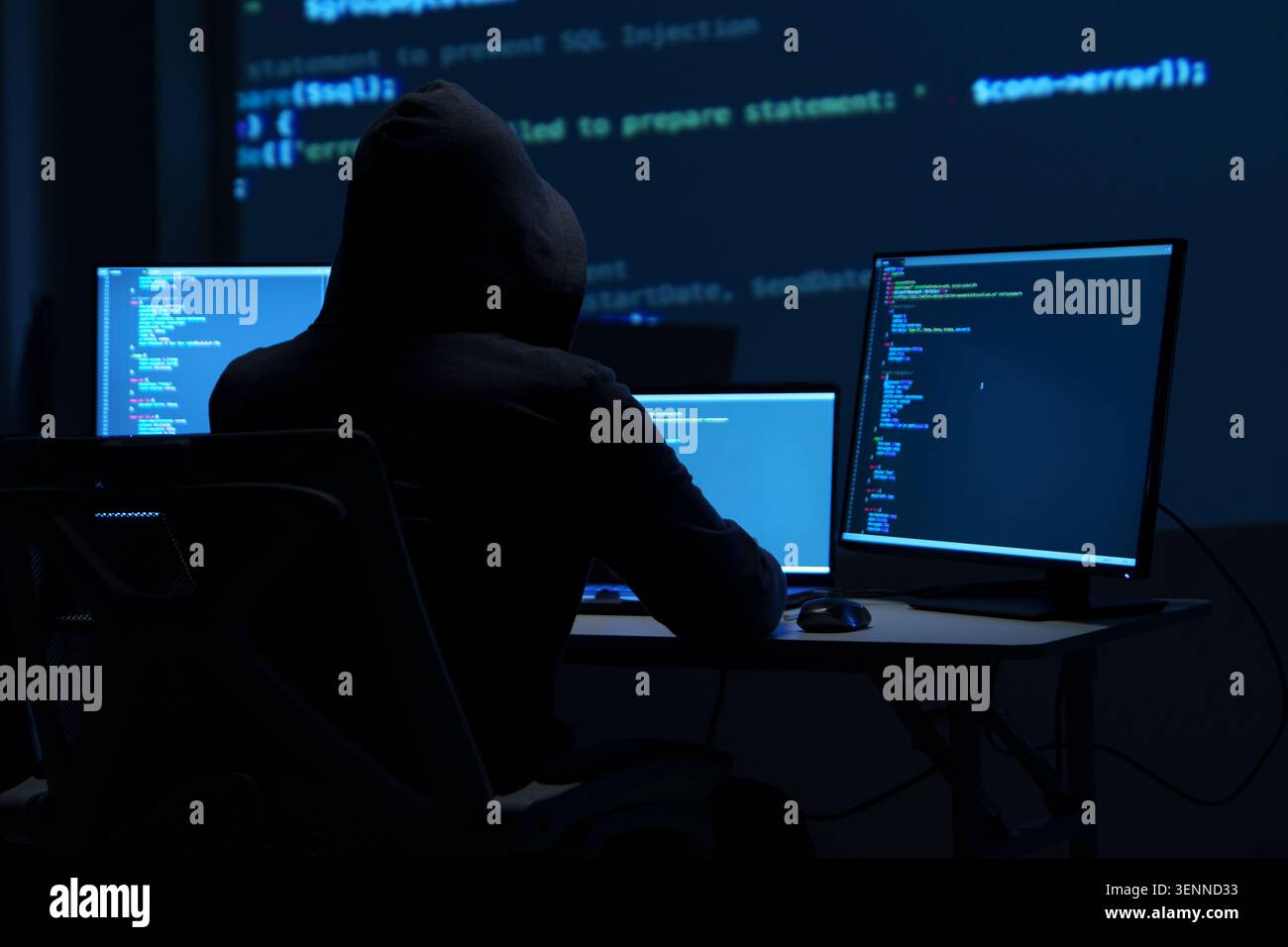 Programmer Hacker Working at Multiple Monitors in Dark Room Stock Photo