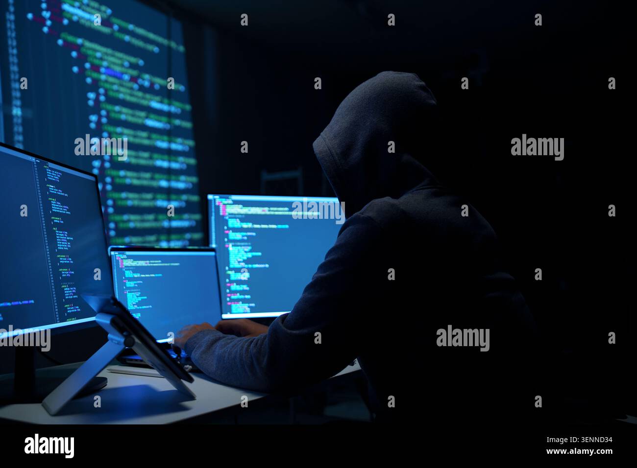 Hacker in Hoodie Working on Multiple Monitors at Night Stock Photo