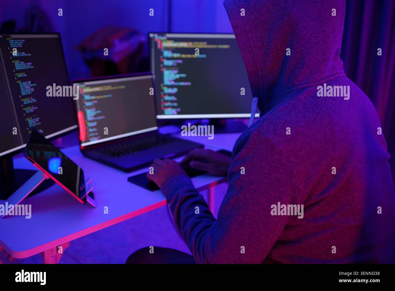 Hacker Coding at MultiMonitor Desk in Neon Light Stock Photo
