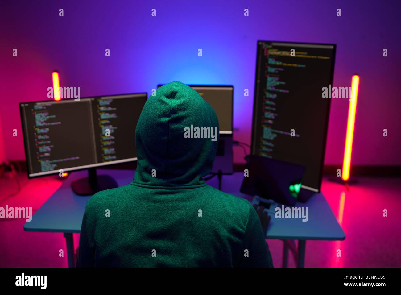 Hooded programmer working at multiple monitors in neon light Stock Photo