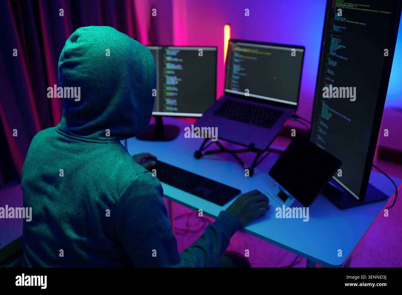 Hacker in Hoodie Working at MultiMonitor Coding Setup Stock Photo