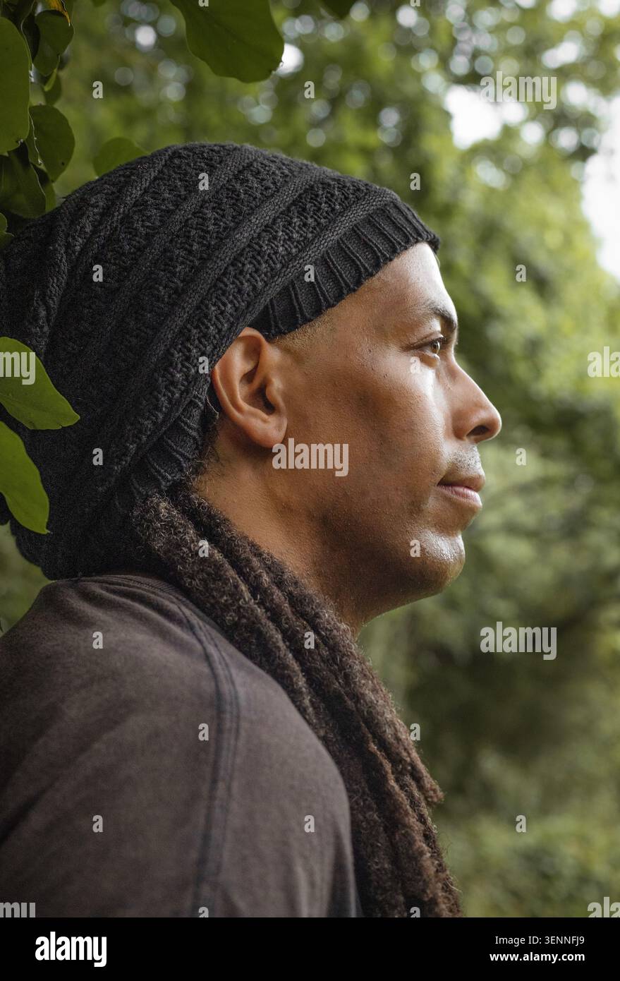 Thoughtful man with dreadlocks standing under a tree Stock Photo