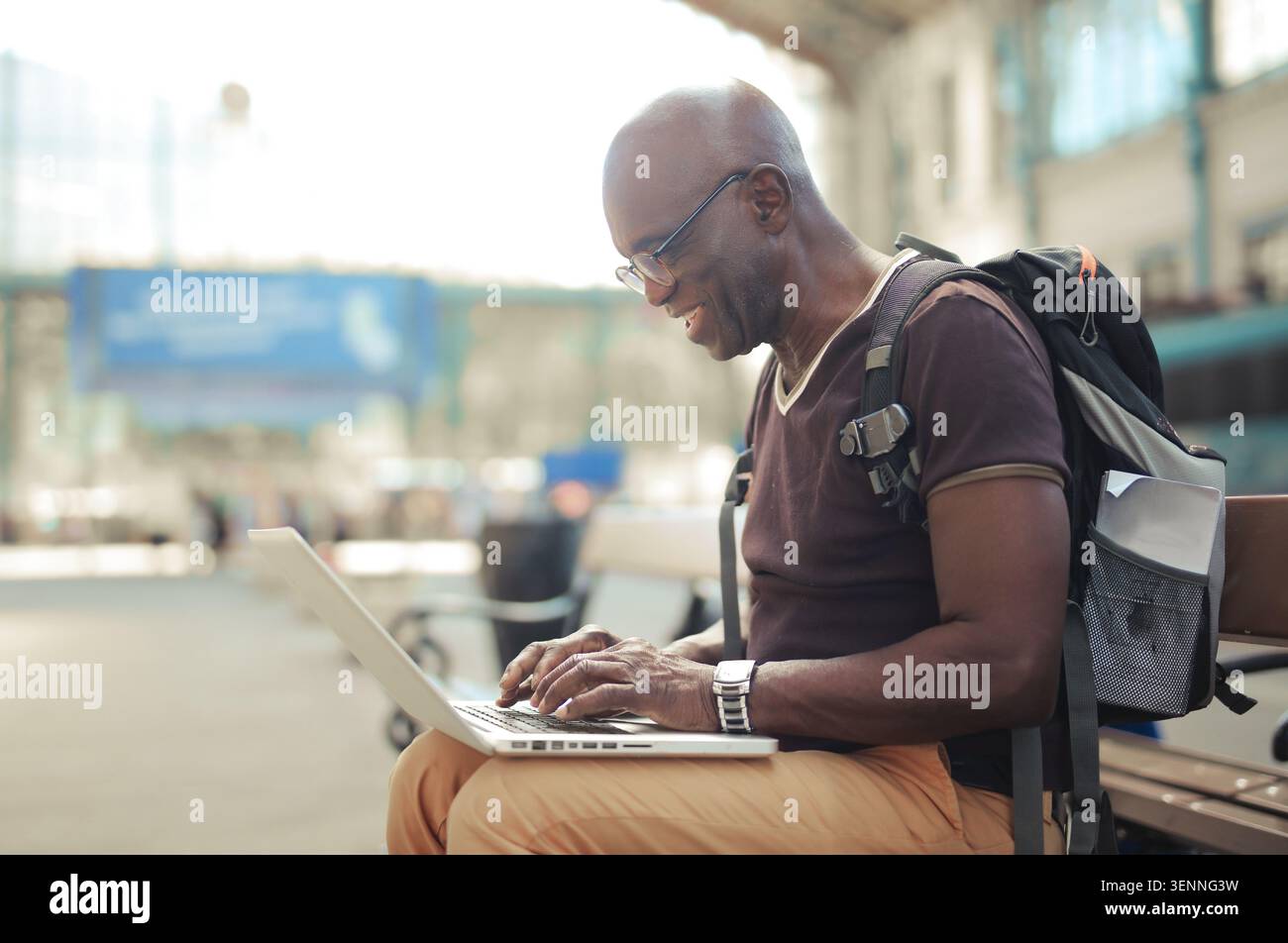 Smiling senior man using laptop at train station Stock Photo