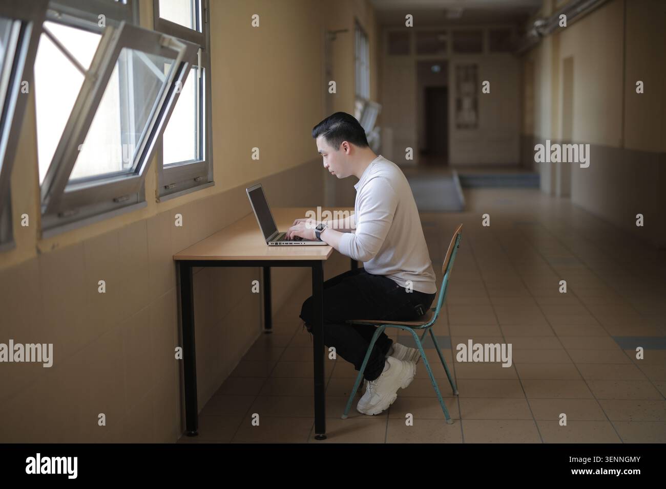 Young Asian man focused on laptop in hallway Stock Photo