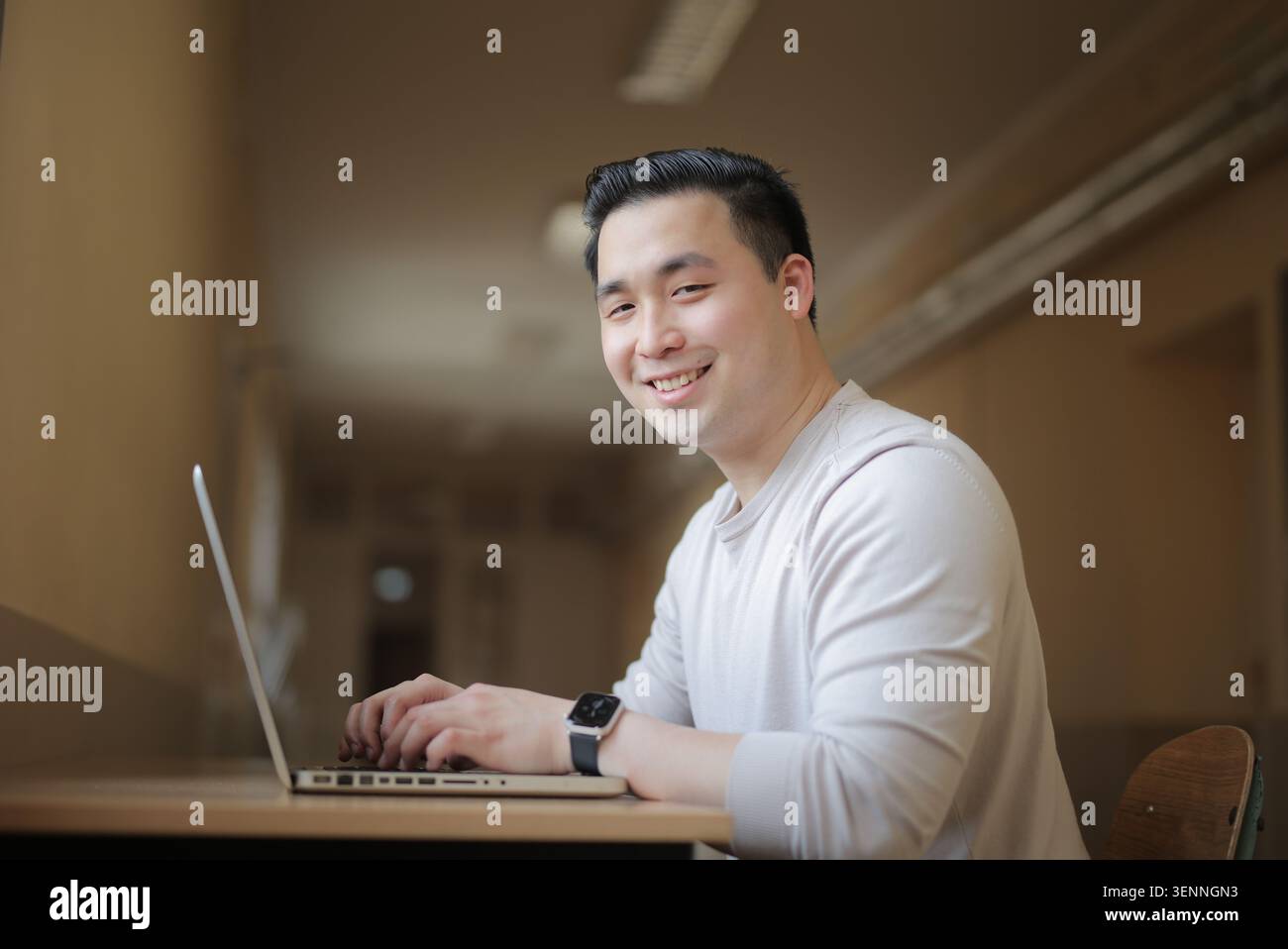 Smiling Asian man looks at camera while using laptop Stock Photo