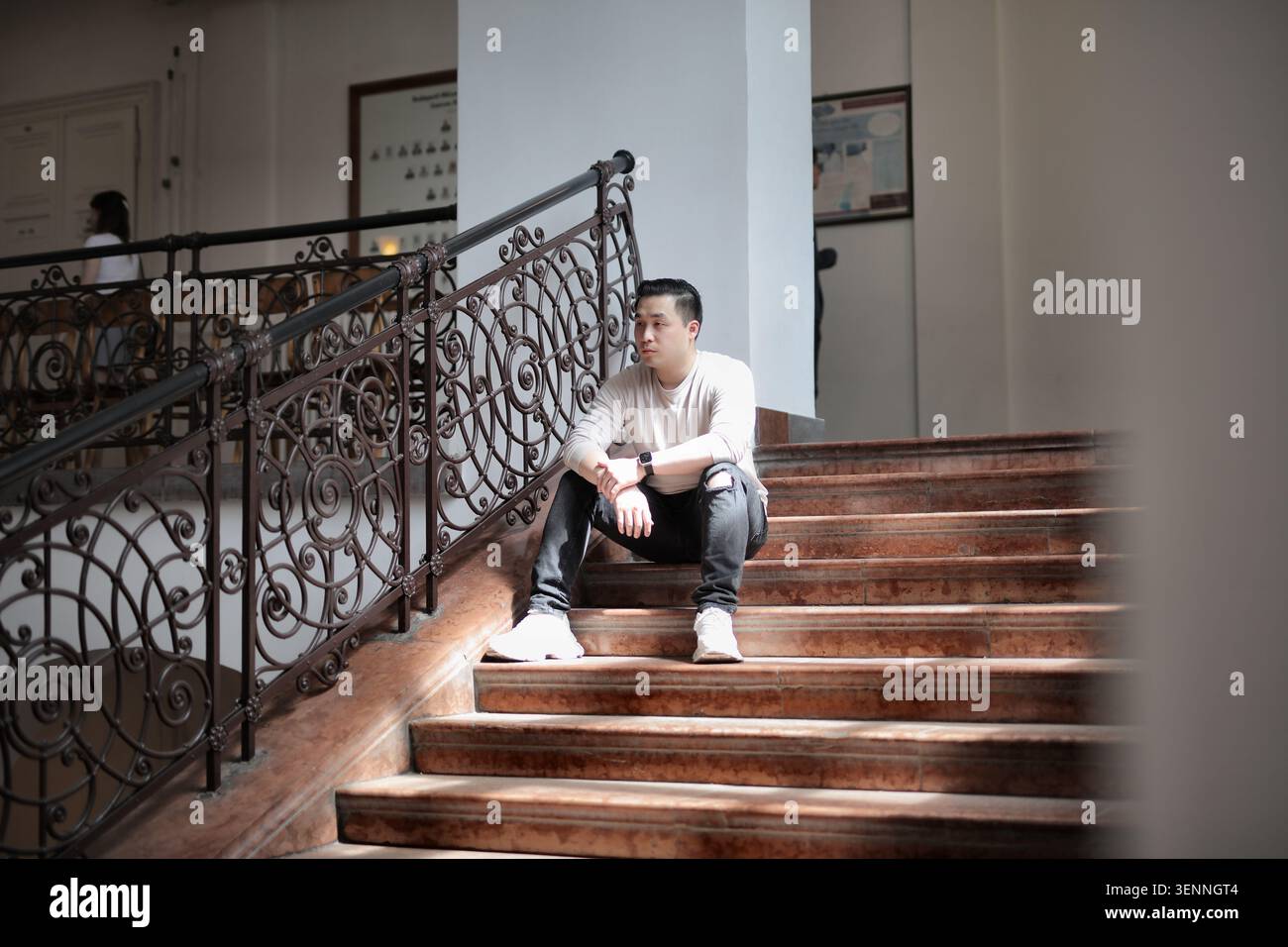 Thoughtful young man sits on a grand staircase Stock Photo