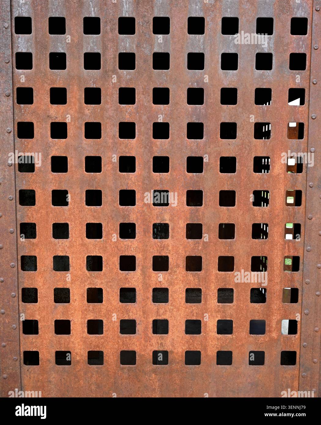 Vertical close up of a rust coated perforated metal panel with square cut out holes and vertical rivets on both sides Stock Photo