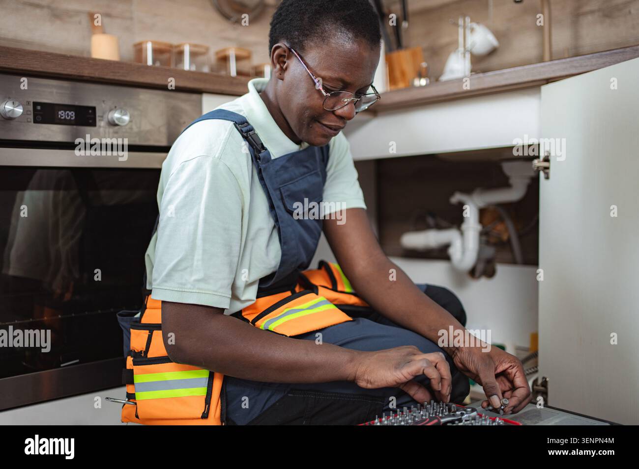 Female plumber fixing pipes under kitchen sink Stock Photo