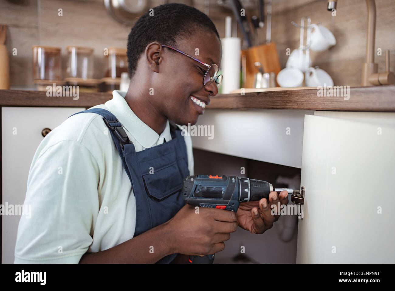 Handyman using cordless screwdriver repairing kitchen cabinet Stock Photo