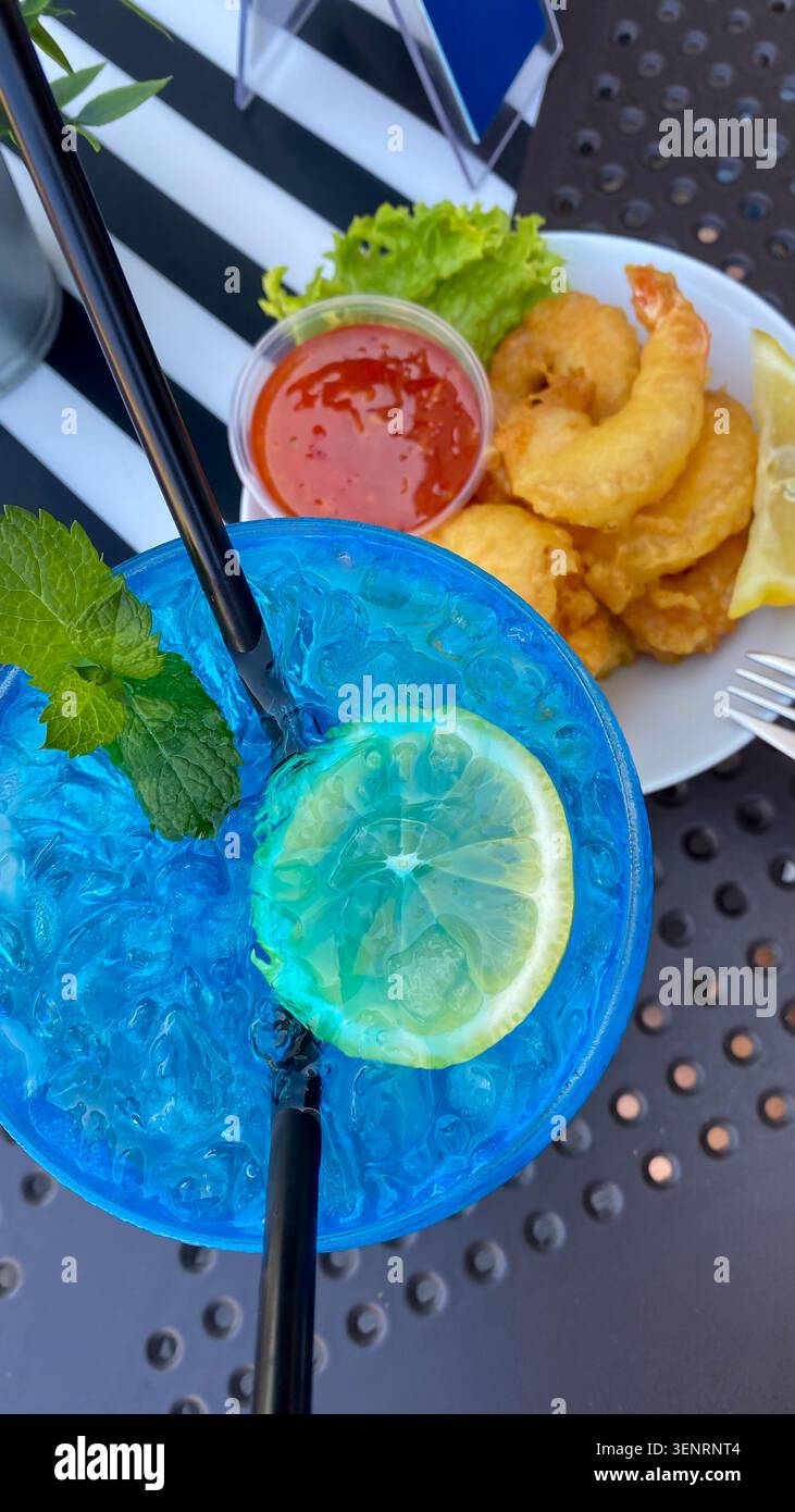 Blue cocktail with lemon and mint next to fried shrimp and sauce Stock Photo