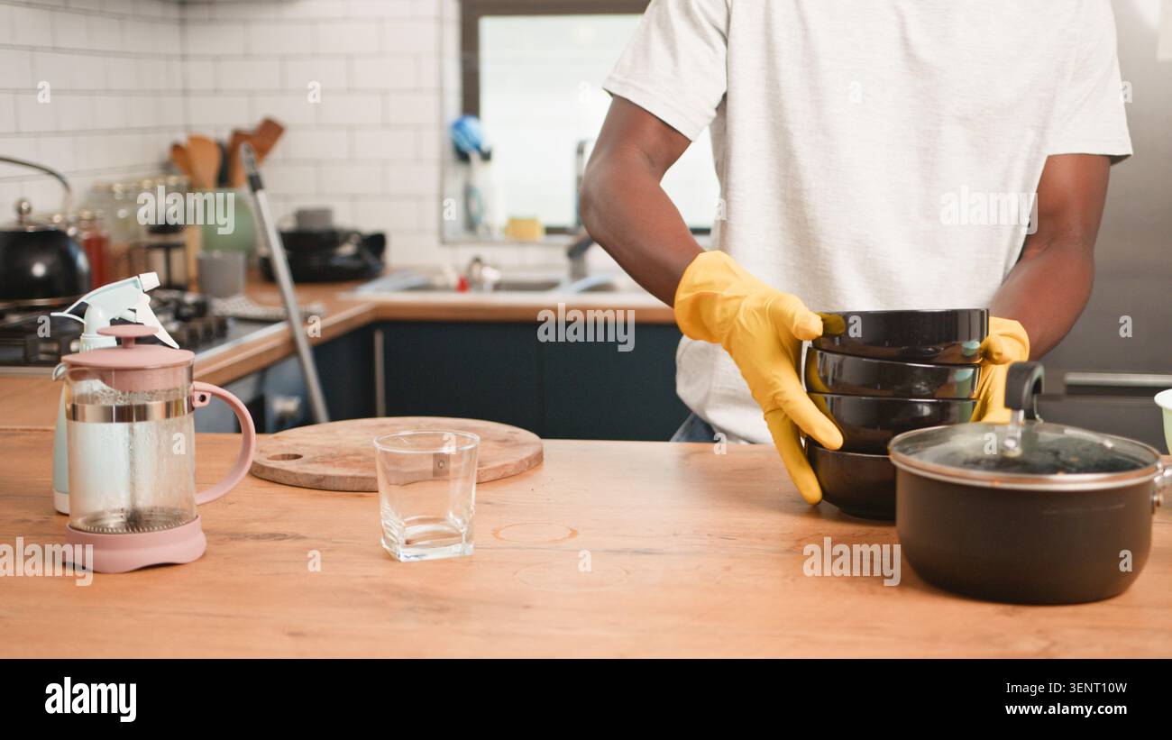 Man Washing Dishes In Modern Kitchen Wearing Yellow Gloves While Stacking Bowls On Counter Stock Photo