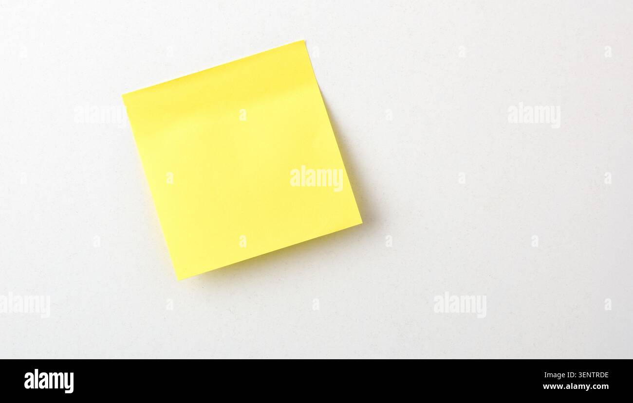 Single yellow sticky note placed on a clean white surface with copy space. Minimal office concept, top view, simple organization and reminder theme. Stock Photo
