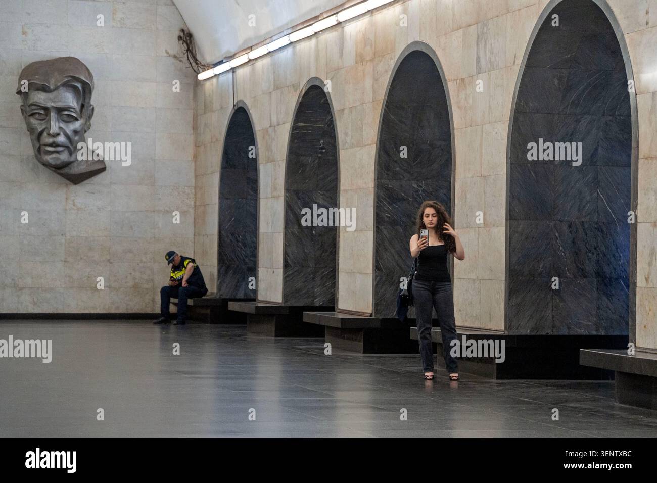 A woman takes a selfie in a subway station while a police offer looks at his phone in Tbilisi, Georgia. Stock Photo