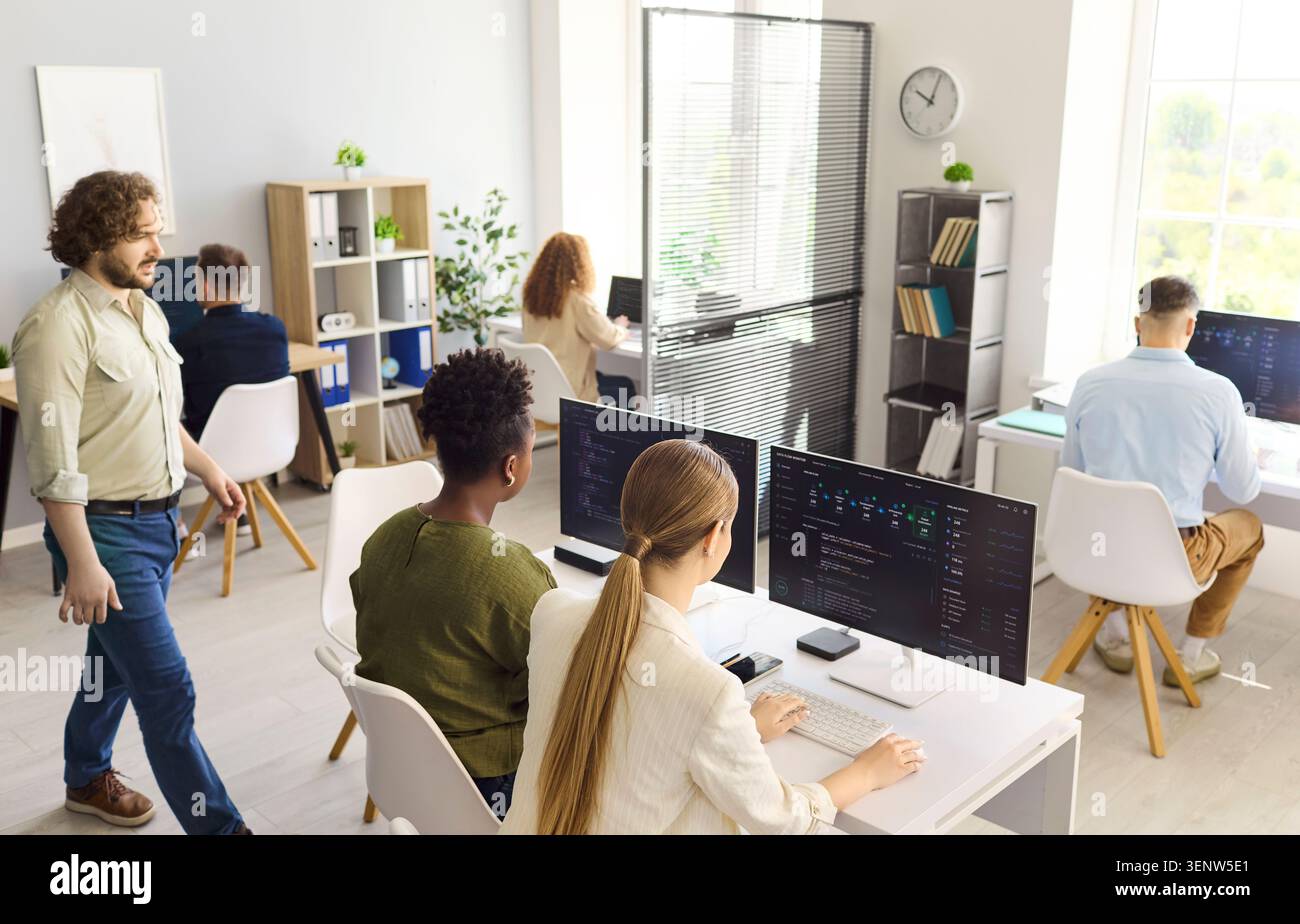 Programmers collaborating in open office workspace, coding software on computers Stock Photo