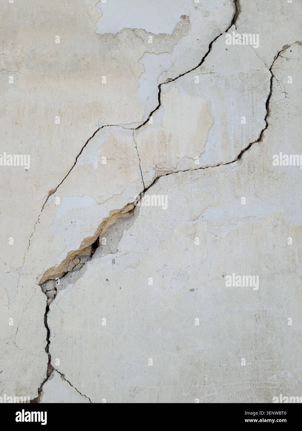 Two diagonal cracks on old white worn concrete wall. Earthquake effects. Selective focus. Stock Photo