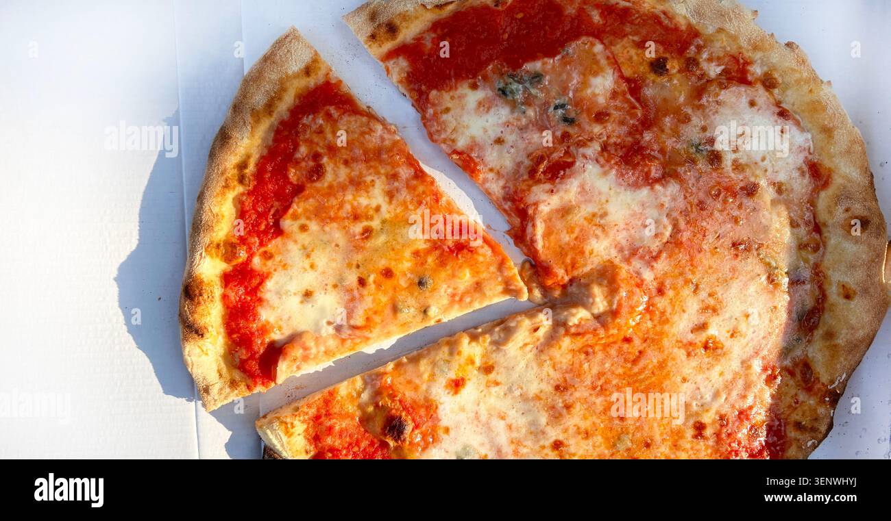 Top view of a fresh, hot classic Margherita pizza with melted molted mozzarella in a cardboard delivery box, with one slice separated. Overhead view. Stock Photo