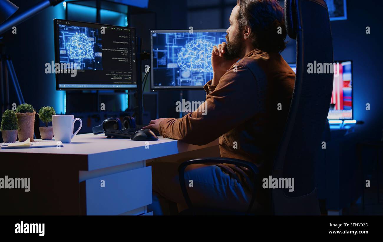 Freelancing programmer writes code on desktop PC to visualize artificial intelligence neural networks, self employed man runs AI script on computer from apartment office, jib down shot. Stock Photo