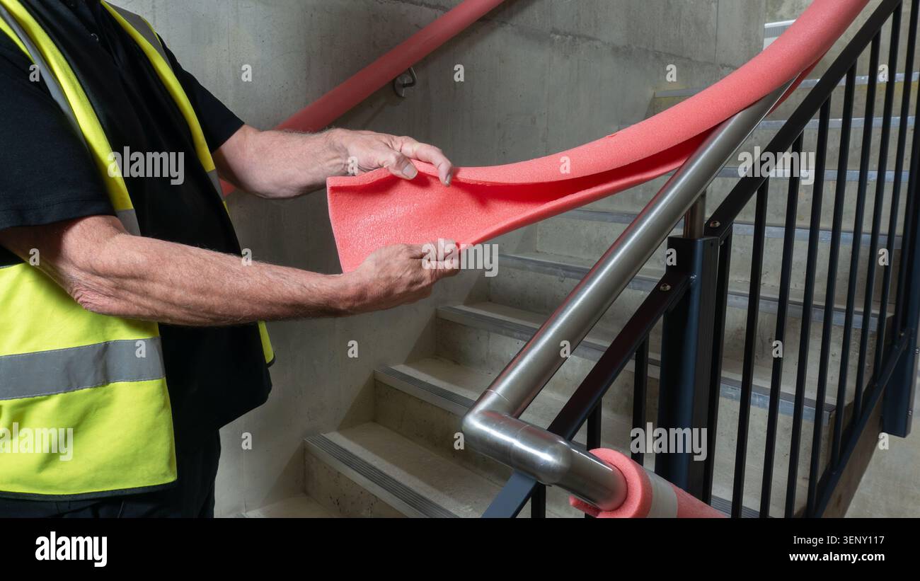 Quality control surveyor inspecting handrail guard covers on an industrial stairwell. Construction engineer removing foam handrail covers at the end Stock Photo