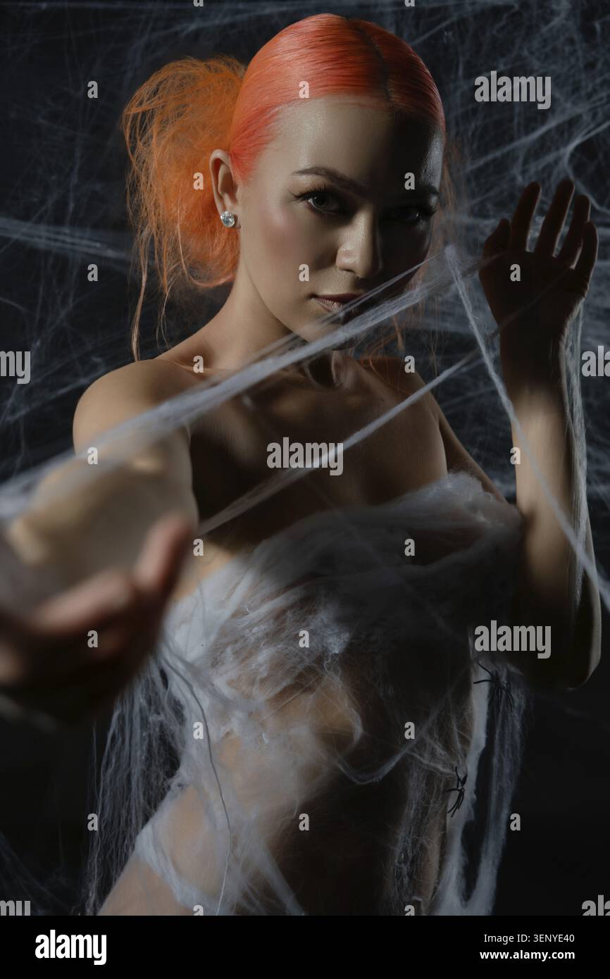 A striking red-haired woman is ensnared in a web, blending beauty and tension in a captivating scene Stock Photo
