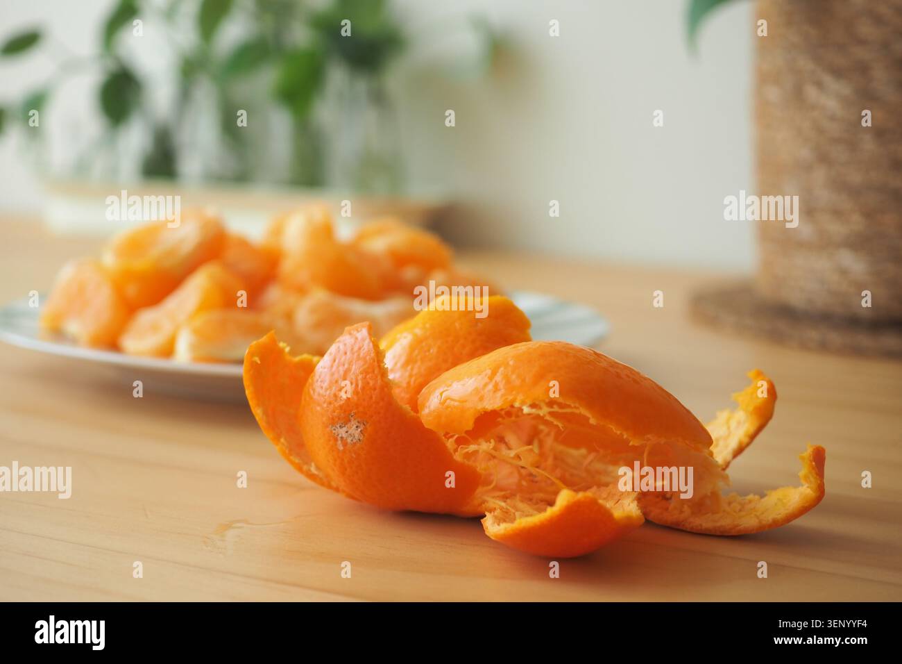 Peeled orange sits on table with more oranges in background Stock Photo