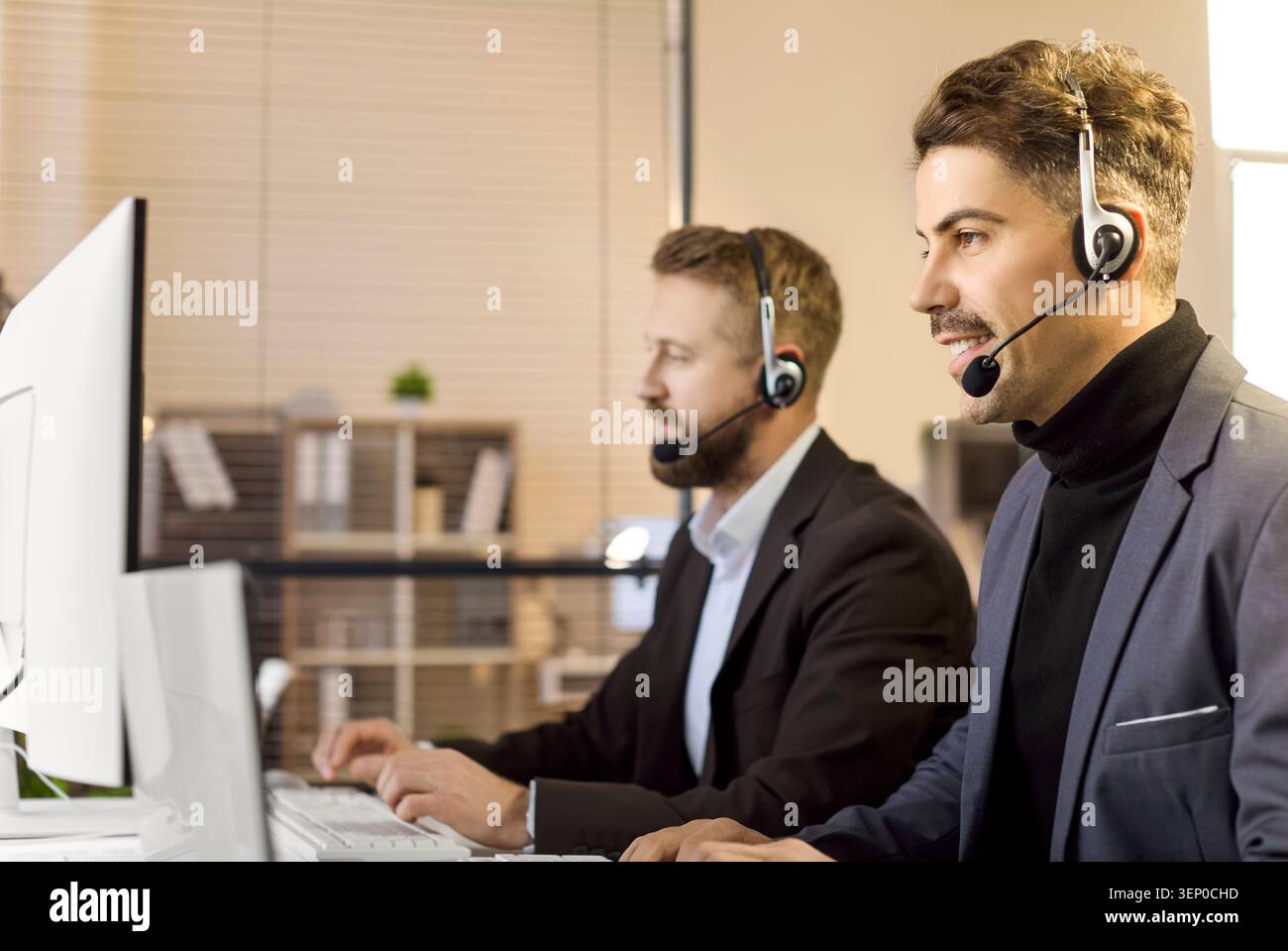 Two call center agents with headsets at office computers, providing support Stock Photo