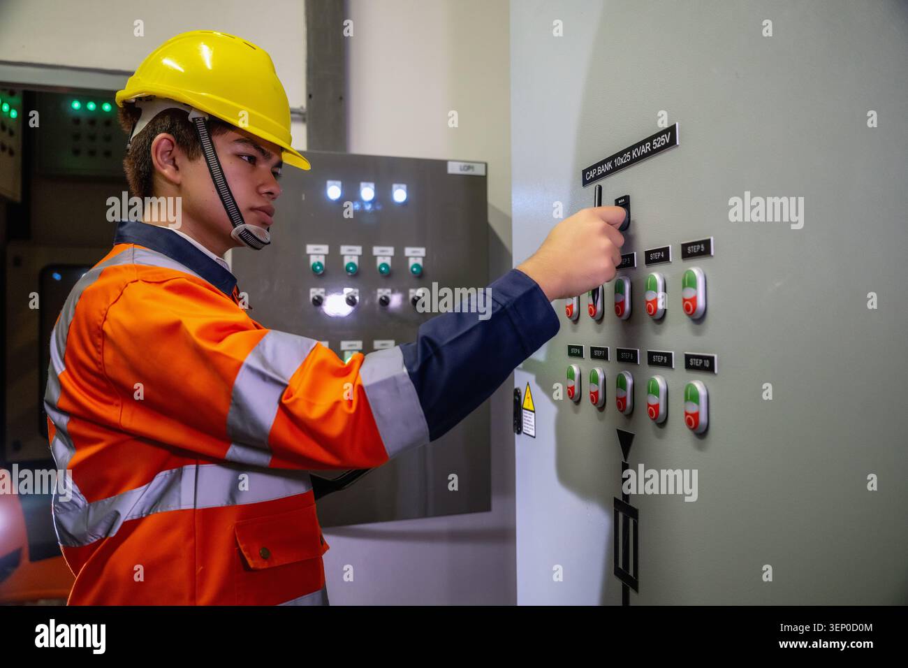 Asian industrial worker turning switch on industrial control panel switchboard, checks control panel inside industrial control room. Control panel has Stock Photo