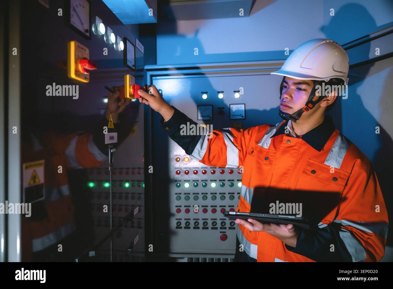 Young electrical engineer holding tablet operating main isolator switch panel, turning disconnector switch power station in control room Stock Photo