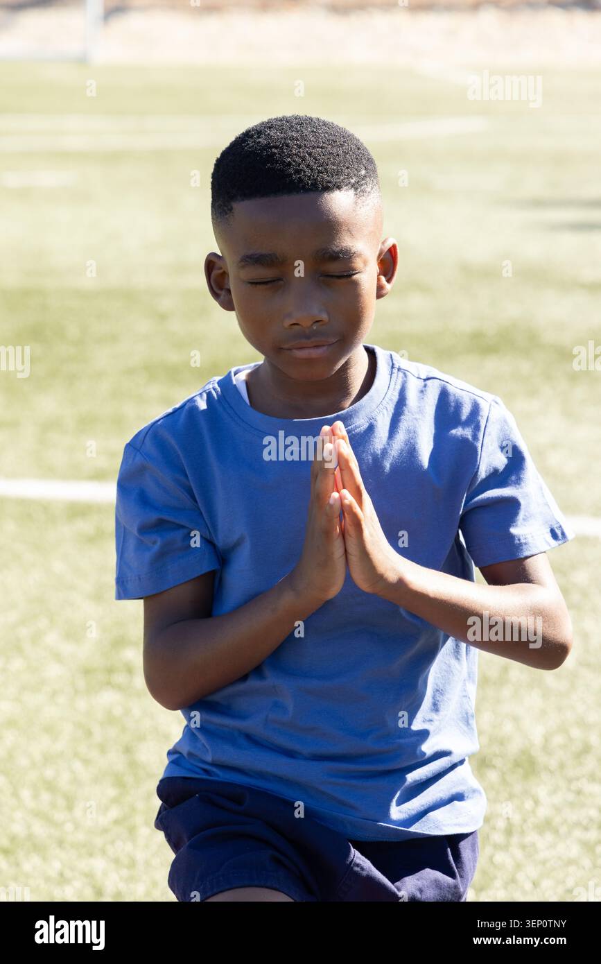 African American schoolboy praying with hands pressed to chest on artificial turf with white lines Stock Photo